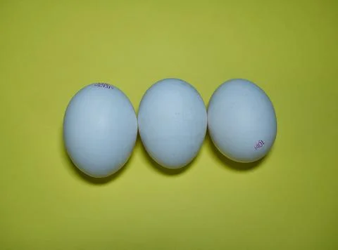 Three white bio eggs on yellow background, topview Foto stock