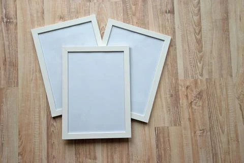 Three white blank frames on the wooden background. Mockup concept. Stock Photos