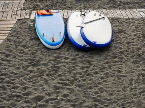 Three white-blue stand up paddle boards lie on the beach with gray sand and 스톡 사진