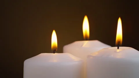 Three white candles are burning on a brown background. taken in close-up. Stock Footage 255057707