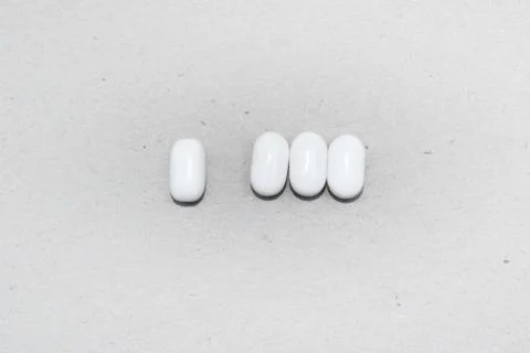 Three white capsules on a white background and a single capsule aside Stock Photos