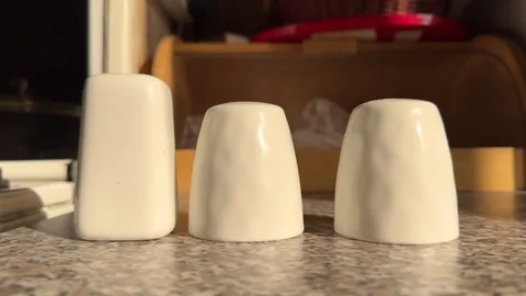 Three white ceramic salt and pepper shakers in the kitchen under the sun rays Stock Footage 306725785