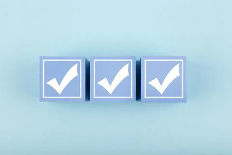 Three white checkmarks on blue cubes against bright pastel blue background Stock Photos