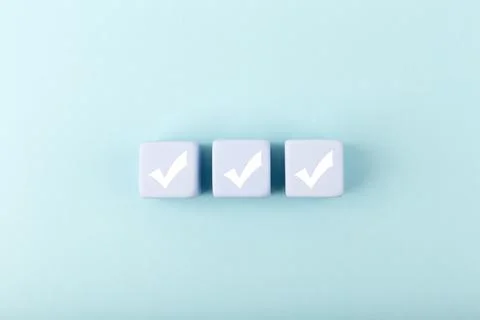 Three white checkmarks on blue toy cubes in a row on bright pastel blue Stock Photos