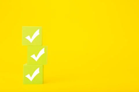 Three white checkmarks drawn on light green toy cubes against bright yellow Stock Photos