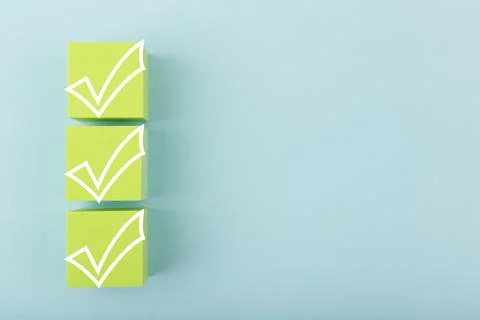 Three white checkmarks on green cubes against bright pastel blue background with Stock Photos