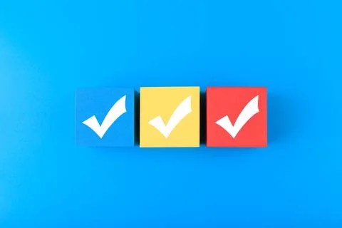 Three white checkmarks on multicolored cubes in a row against blue background Stock Photos