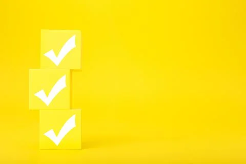 Three white checkmarks on yellow toy cubes against bright yellow background with Stock Photos
