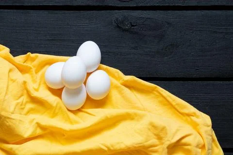 Three white chicken eggs on a bright yellow cloth on a black wooden board, de Stock Photos