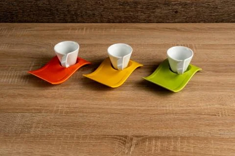 Three white coffee cups placed on orange, yellow, gren plates Foto stock
