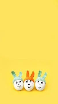 Three white eggs in beanie with rabbit ears and cheerful faces on yellow Stock Photos