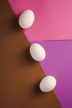 Three white eggs in diagonal row on purple, pink and brown colors Stock Photos
