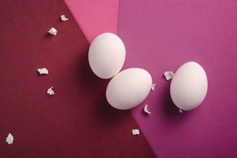 Three white eggs with eggshell pieces on red, pink and purple colors Stock Photos