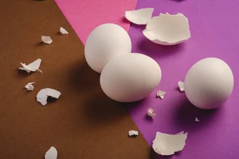 Three white eggs with eggshell pieces on purple, pink and brown colors Stock Photos