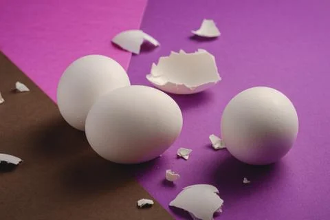 Three white eggs with eggshell pieces on purple, pink and brown colors Stock Photos