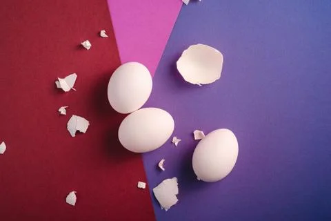 Three white eggs with eggshell pieces on red, pink and blue colors Stock Photos