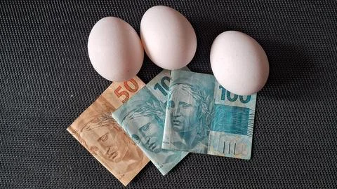 Three white eggs resting on top of Brazilian paper money banknotes Stock Photos