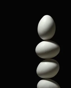 Three white eggs stacked in tall column on black background forming dramatic Fotos Stock