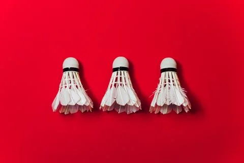 Three White Feather Shuttlecocks Arranged In A Row Against A Bold Red Background Foto stock