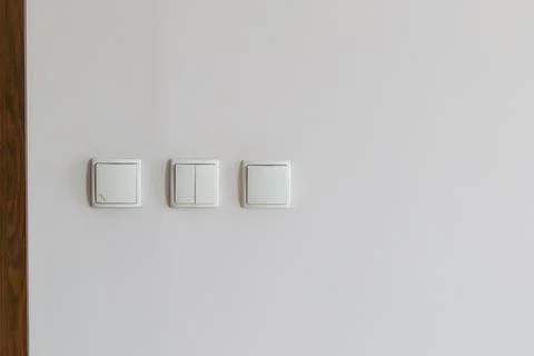 Three white light switches on a light wall Stock Photos