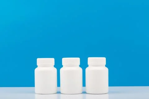 Three white medication bottles against blue background. Concept of vitamins Stock Photos