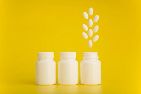 Three white medication bottles with the last one opened with pills jumping out Stock Photos