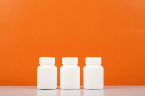 Three white medication bottles in a row against orange background with copy Foto stock