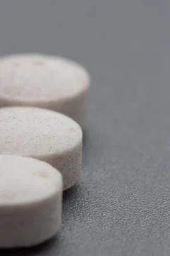 Three white pills sit in a row on a gray surface Stock Photos