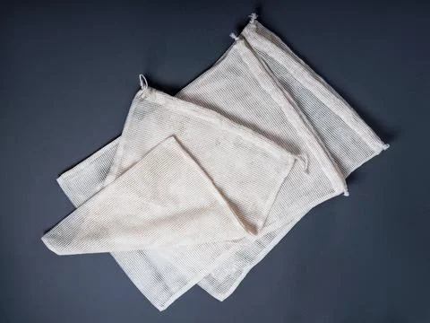 Three white reusable string bags for different products on the grey background. Stock Photos
