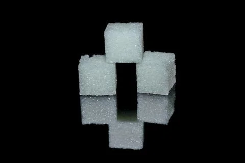 Three white sugar cubes from crystals on black glossy glass Stock Photos
