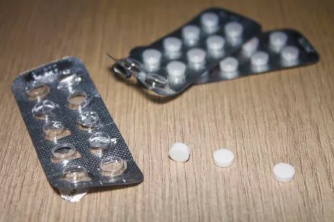 Three white tablets and empty packaging lie on a wooden surface. Stock Photos
