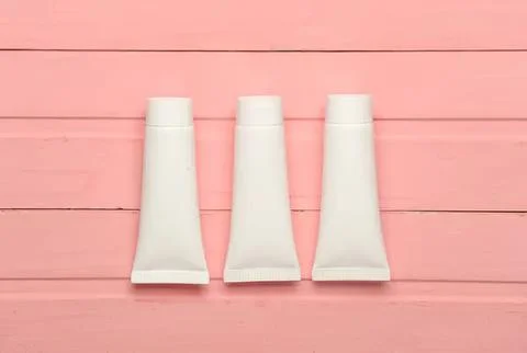 Three white toothpaste tubes on pink wooden surface Fotos Stock