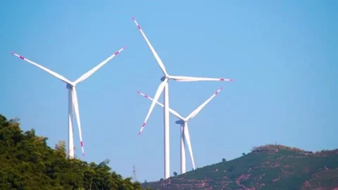 Three white wind turbines rotating on green mountain under blue sky. Stock Footage 336333792