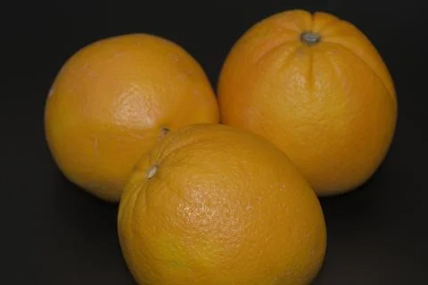Three whole fresh oranges grouped on a dark black background Stock Photos