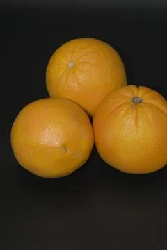 Three whole fresh oranges grouped on a dark black background Stock Photos