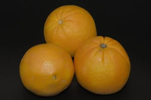 Three whole fresh oranges grouped on a dark black background Stock Photos
