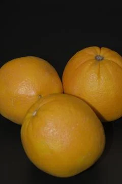 Three whole fresh oranges grouped on a dark black background Stock Photos