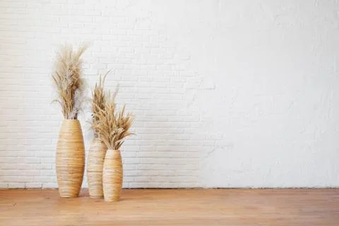 Three wicker vases with dry pampas grass against a white textured brick wall. Stock Photos