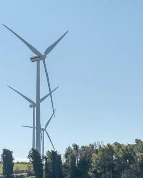 Three wind turbines almost lined up behind a forest Stock Photos