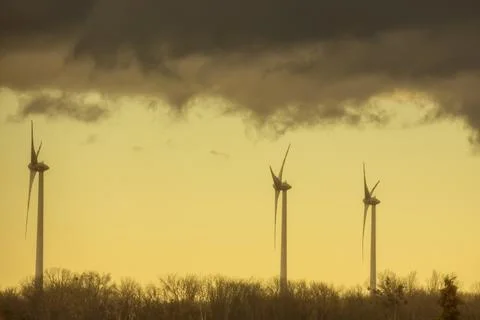 Three windmills in a flat landscape with dark rainclouds and yellow color Foto stock