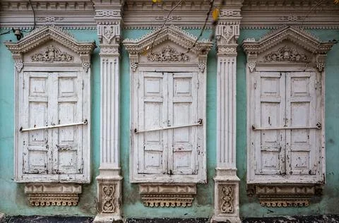 Three windows with closed shutters of old house with carved decor and stucco Stock Photos