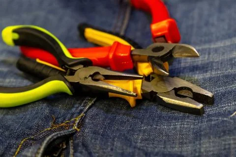 Three wire cutters bright plastic green handles red yellow on jeans backgroun Stock Photos