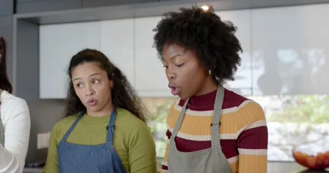 Three women in aprons discussing steps shaping dough on kitchen island placing Stock Footage 340655231