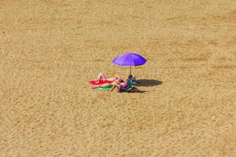 Three women are sunbathing on an empty beach under an umbrella on a sunny s.. Stock Photos