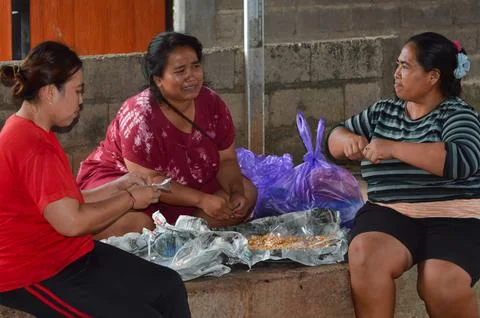 Three women chatting while packaging fried peanuts into plastic bags 스톡 사진