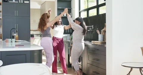 Three women joining hands and swaying in kitchen by island, window while sharing Stock Footage 342928465