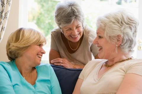 Three women in living room talking and smiling Stock Photos