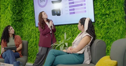 Three women presenting data in lounge, presenter holding mic, gesturing to 50% Stock Footage 338009054
