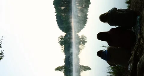 Three women sitting by the river at dawn, their silhouettes softly illuminated Stock Footage 309408948