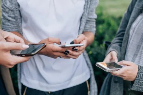 Three women's hands are using mobile phone at the park. Stock Photos